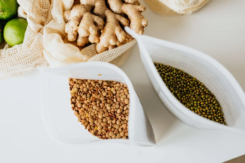 Lentily, čo je vitamín B1: fazole v sáčcích vedle čerstvého zázvoru na bílém pozadí.