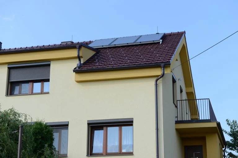 Žlutý dům s fotovoltaickými panely na střeše pod modrou oblohou.