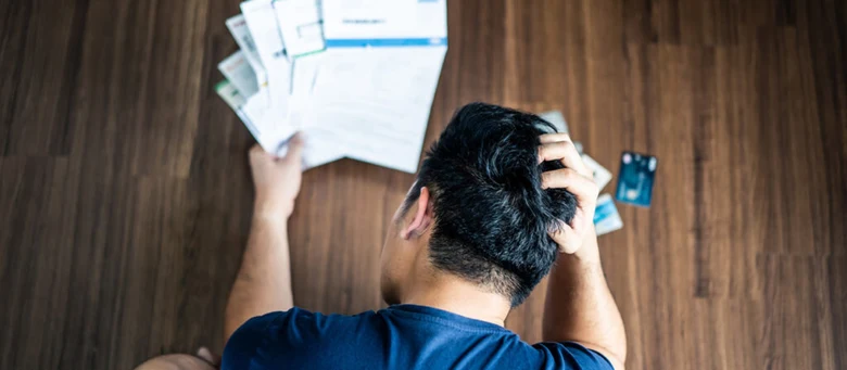 Muž sedí na podlaze s papíry a kartami pro konsolidaci dluhů.