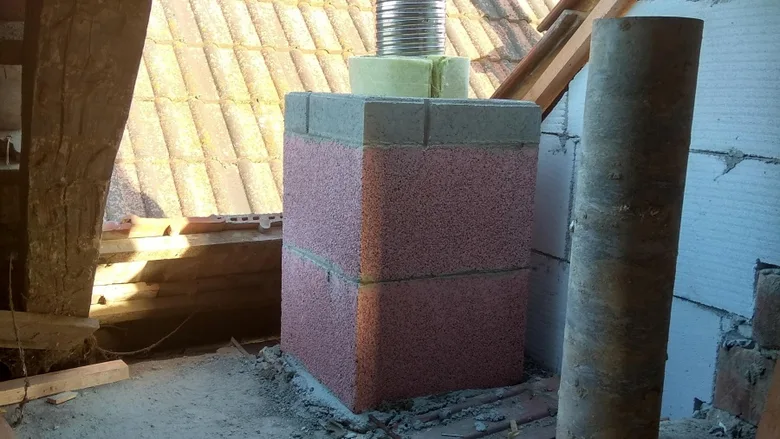 Komín vložovaný růžovými izolačními bloky ve střeše.
