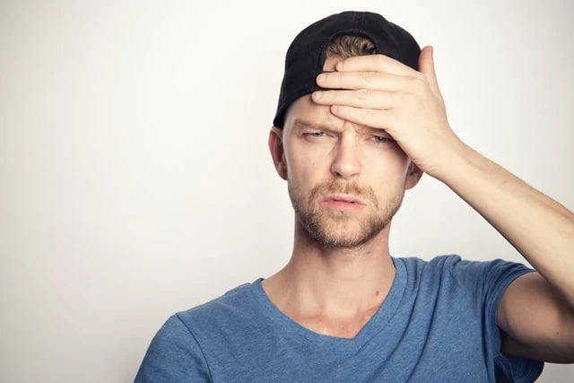 Muž drží ruku na čele jako příznak bolesti hlavy.