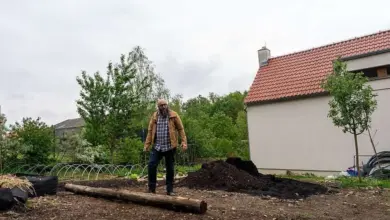 Muž stojí na dřevěném kmeni v zahradním svahu s hromadou zeminy.