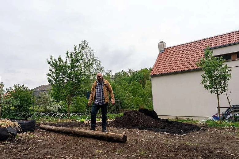 Muž stojí na dřevěném kmeni v zahradním svahu s hromadou zeminy.