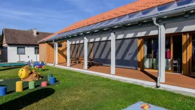 Dům s fotovoltaickými panely na střeše a hřištěm pro děti.