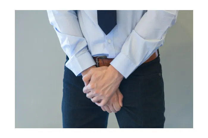 Muž v obleku drží za kříži kvůli bolesti prostaty.