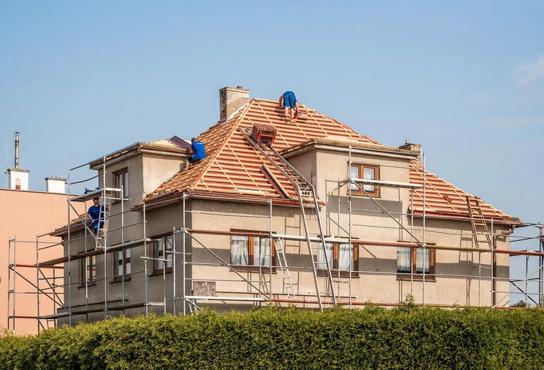 Stavebníci montují novou střechu na rodinném domě.