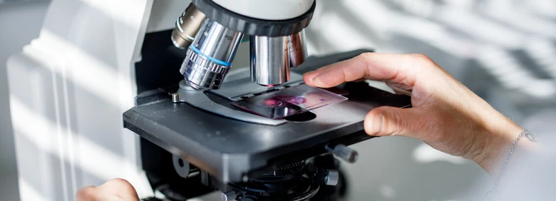 Ruka s mikroskopem pro laboratorní vyšetření vzorku.