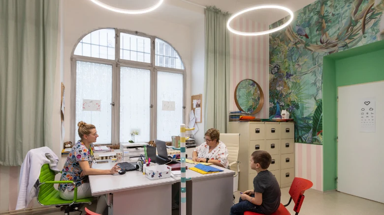 Lékařka konzultuje s malým pacientem v barevném ordinaci.