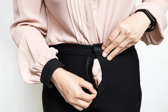 Žena opravuje zip na kalhotách pomocí obou rukou.
