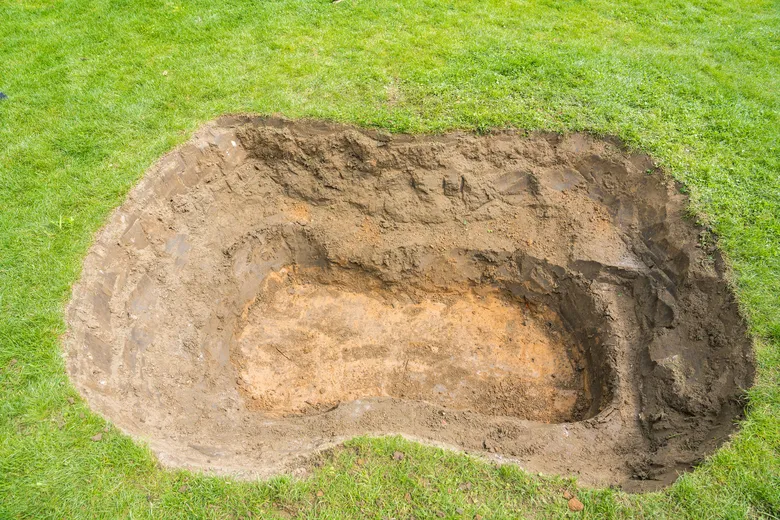 Vykopaná díra pro venkovní koupací jezírko v trávníku.