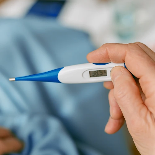 Digitální teploměr v ruce ukazuje horečku při kašli.