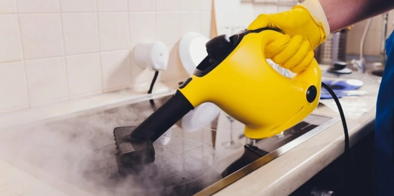 Člověk čistí skleněnou desku parním čističem s výfukem páry.
