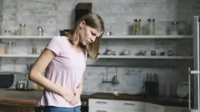 Žena v kuchyni drží břicho kvůli bolesti nebo nadýmání.