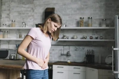 Žena v kuchyni drží břicho kvůli bolesti nebo nadýmání.